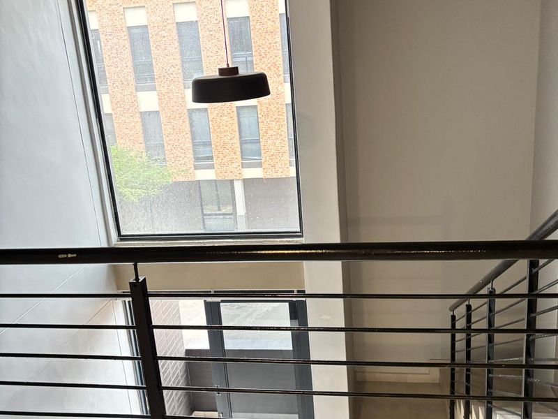 A bright stairwell area featuring a modern metal balustrade, large windows providing natural light, and a contemporary pendant light fixture.
