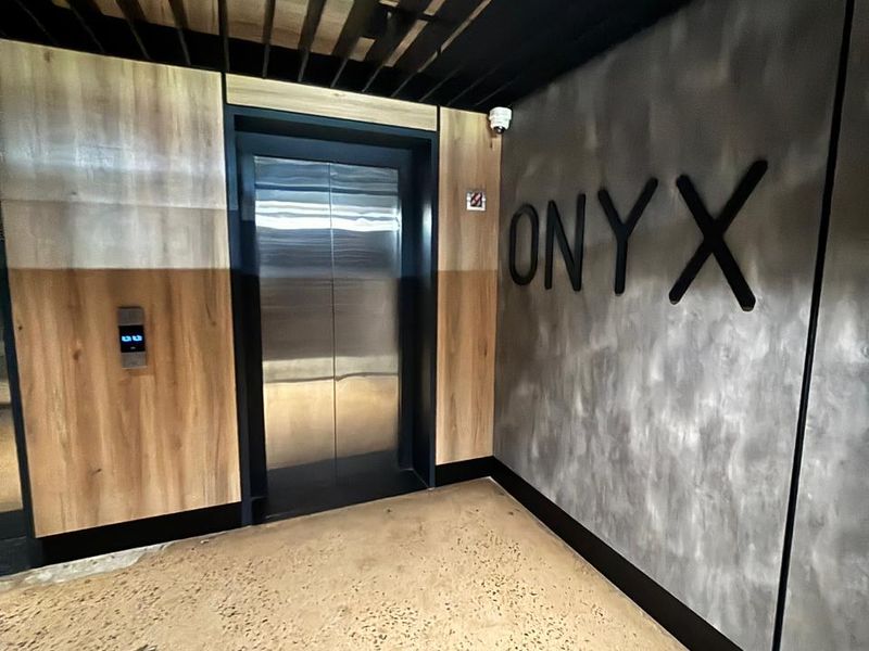 Modern apartment building elevator lobby featuring industrial-style concrete wall, wood paneling, and exposed ceiling structure.