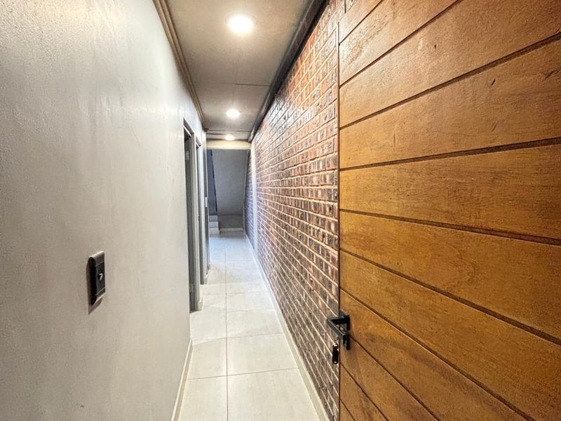 A well-lit hallway featuring a striking exposed brick feature wall, tiled flooring, and a modern timber-panelled door.