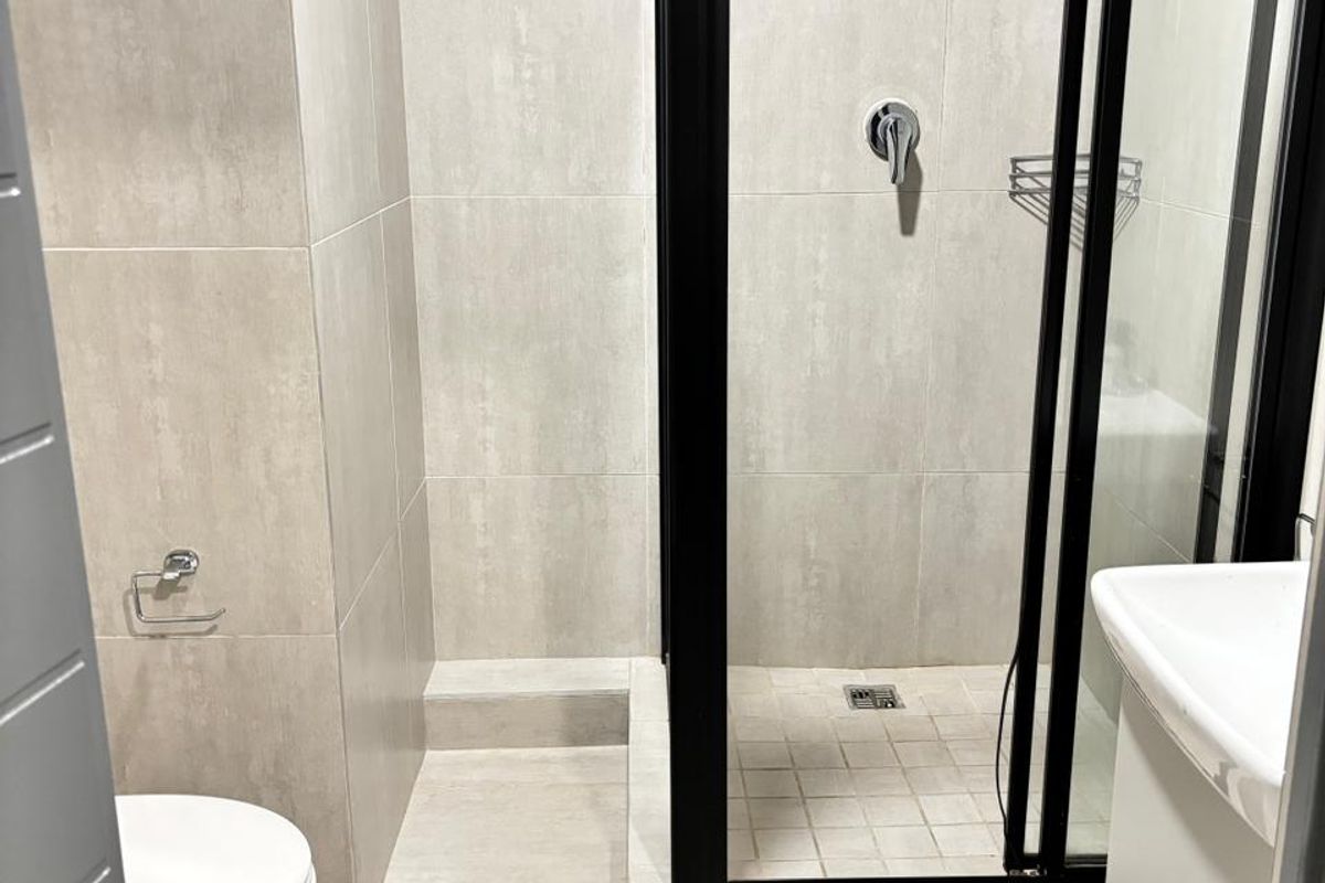 Modern bathroom featuring a walk-in shower with a black frame, neutral floor-to-ceiling tiling, a wall-mounted toilet, and a vanity basin.