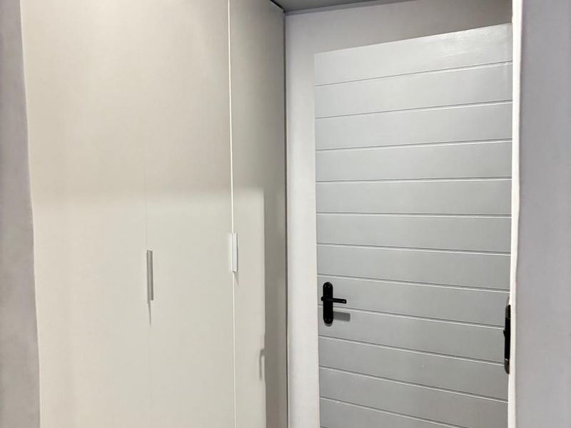 A clean hallway featuring built-in floor-to-ceiling white cabinetry and a modern horizontal-slatted grey door with black hardware.