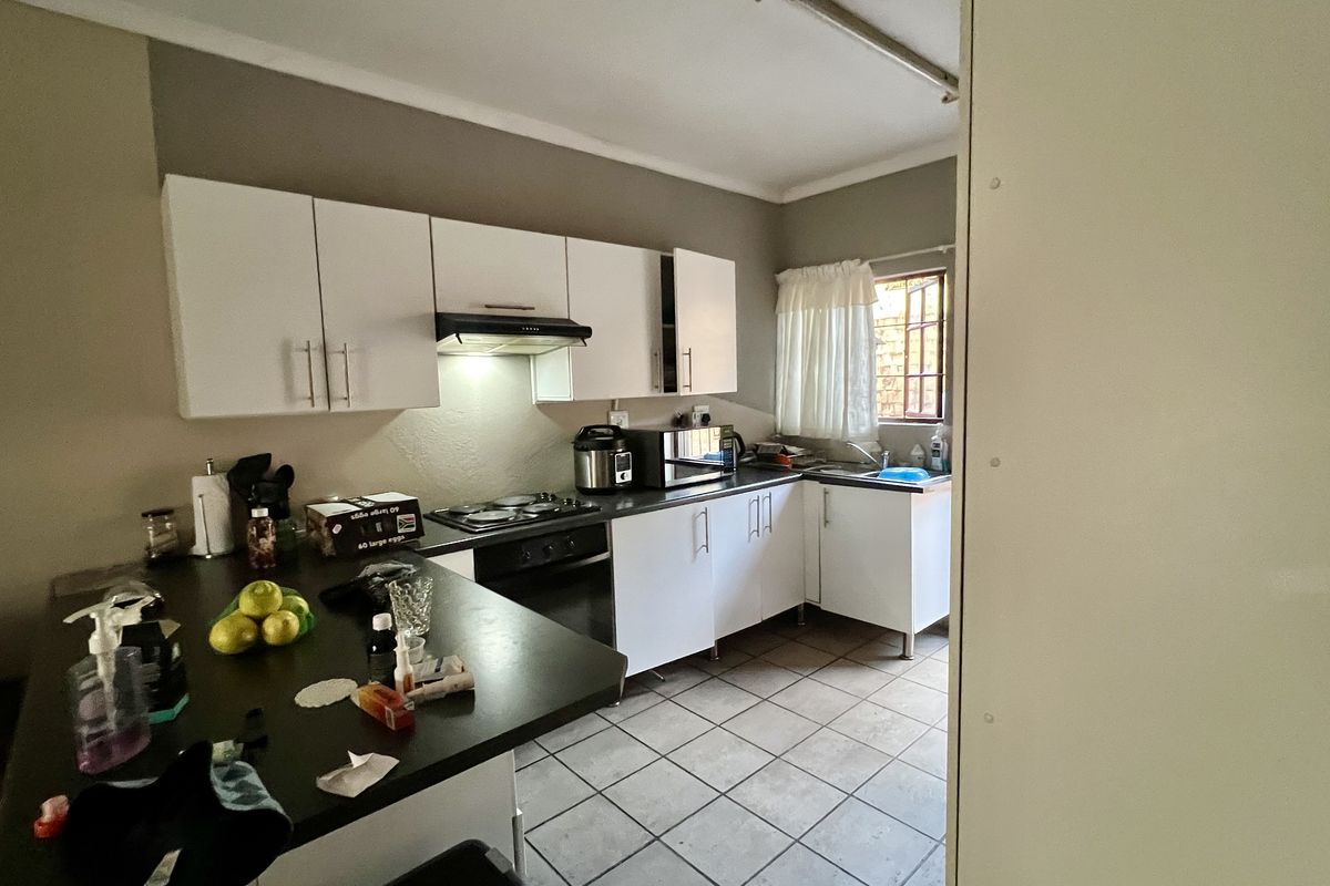 Functional kitchen featuring white cabinetry, dark countertops, built-in hob, extractor fan, and tiled flooring with a window providing natural light.