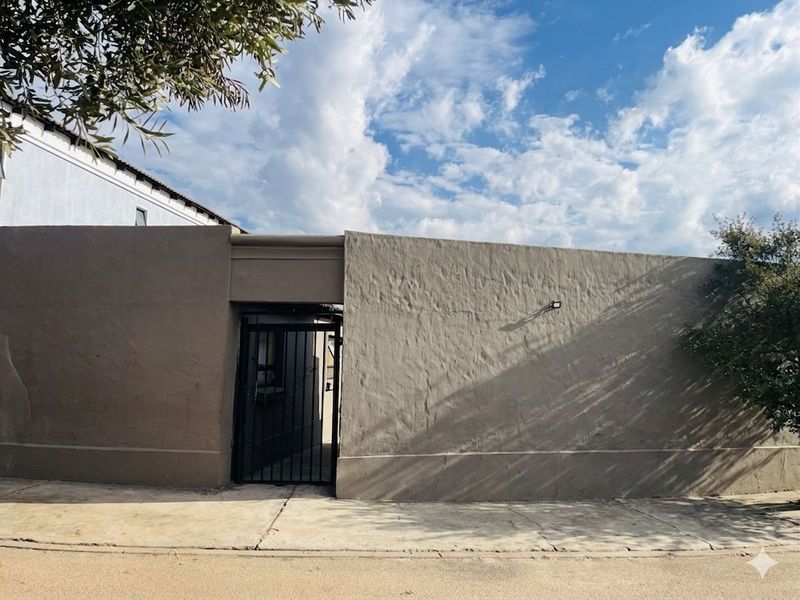 A view of the property's exterior boundary wall featuring a secure metal pedestrian gate and a textured plaster finish.