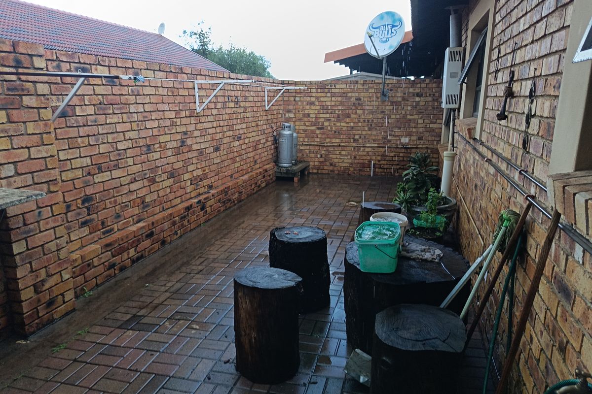 A paved rear courtyard area featuring face-brick walls, wall-mounted washing lines, and an external gas geyser unit.