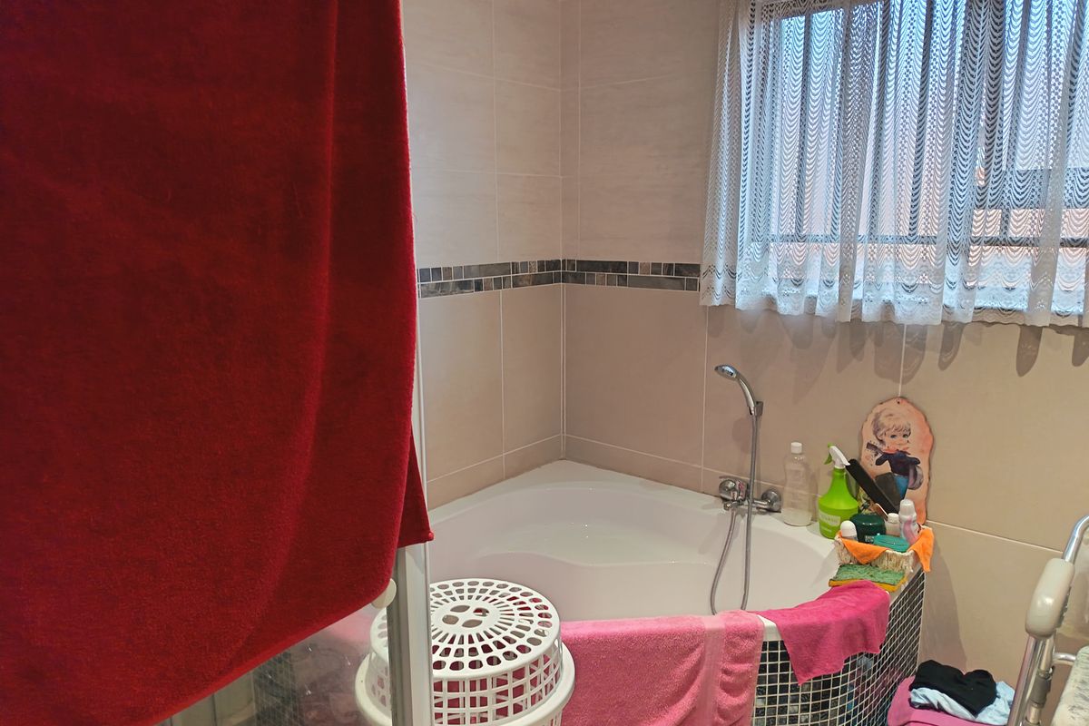 A bathroom featuring a corner bathtub with mosaic tile detailing and wall-mounted shower mixer, complemented by neutral wall tiling.