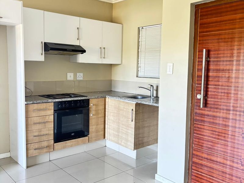 Compact kitchen featuring white upper cabinetry, wood-finish lower cabinets, granite countertops, built-in oven, hob, and extractor fan with tiled flooring.