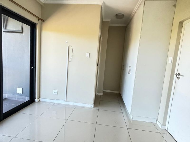 A bright, empty bedroom featuring tiled flooring, built-in cupboards, and a sliding glass door providing access to an outdoor balcony area.