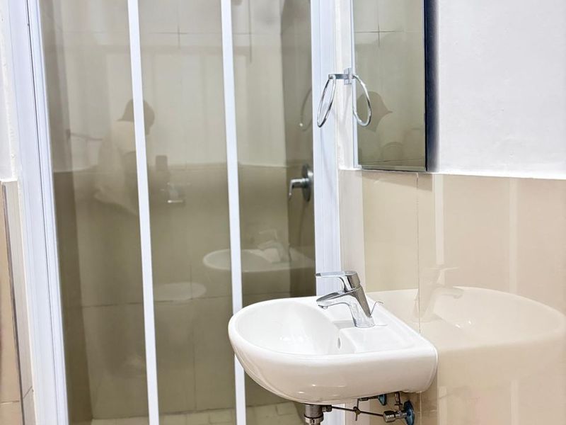 A compact bathroom featuring a wall-mounted basin with chrome tapware, a glass-enclosed shower, and neutral wall tiling.