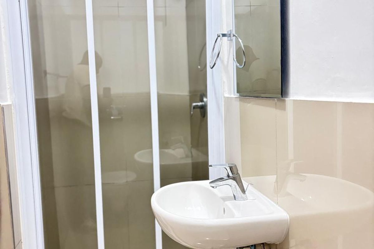 A compact bathroom featuring a wall-mounted basin with chrome tapware, a glass-enclosed shower, and neutral wall tiling.