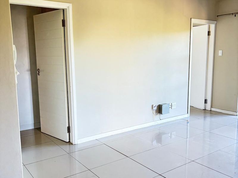 A bright, empty living area featuring neutral wall tones and polished ceramic floor tiles, providing a clean and versatile space.