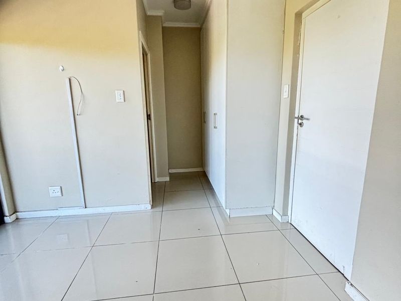 A bright hallway featuring neutral tiled flooring, built-in storage cupboards, and access to adjacent rooms.