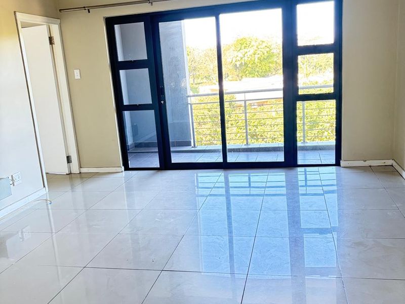 Bright and spacious living area featuring large sliding glass doors that open onto a private balcony, complemented by polished ceramic floor tiles.