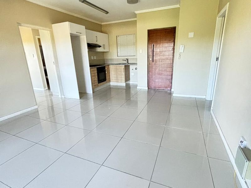 Open plan living area featuring tiled flooring and a compact kitchen with built-in cabinetry, oven, and extractor fan.