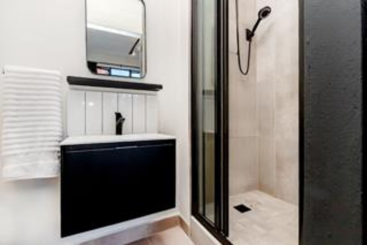 Modern bathroom featuring a sleek black vanity, wall-mounted mirror, and a glass-enclosed shower with contemporary tiling and matte black fixtures.