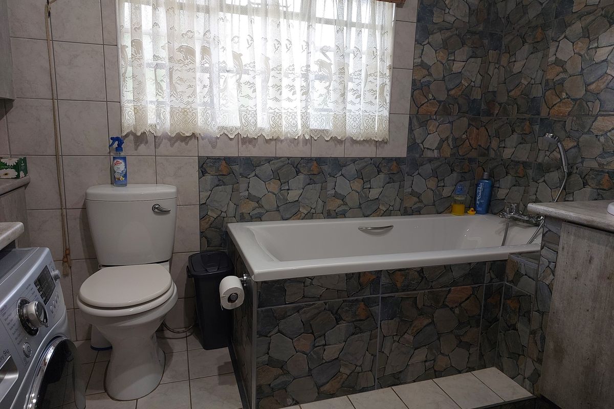 A functional bathroom featuring a built-in bathtub with stone-cladding finish, a standard toilet, and integrated laundry space.