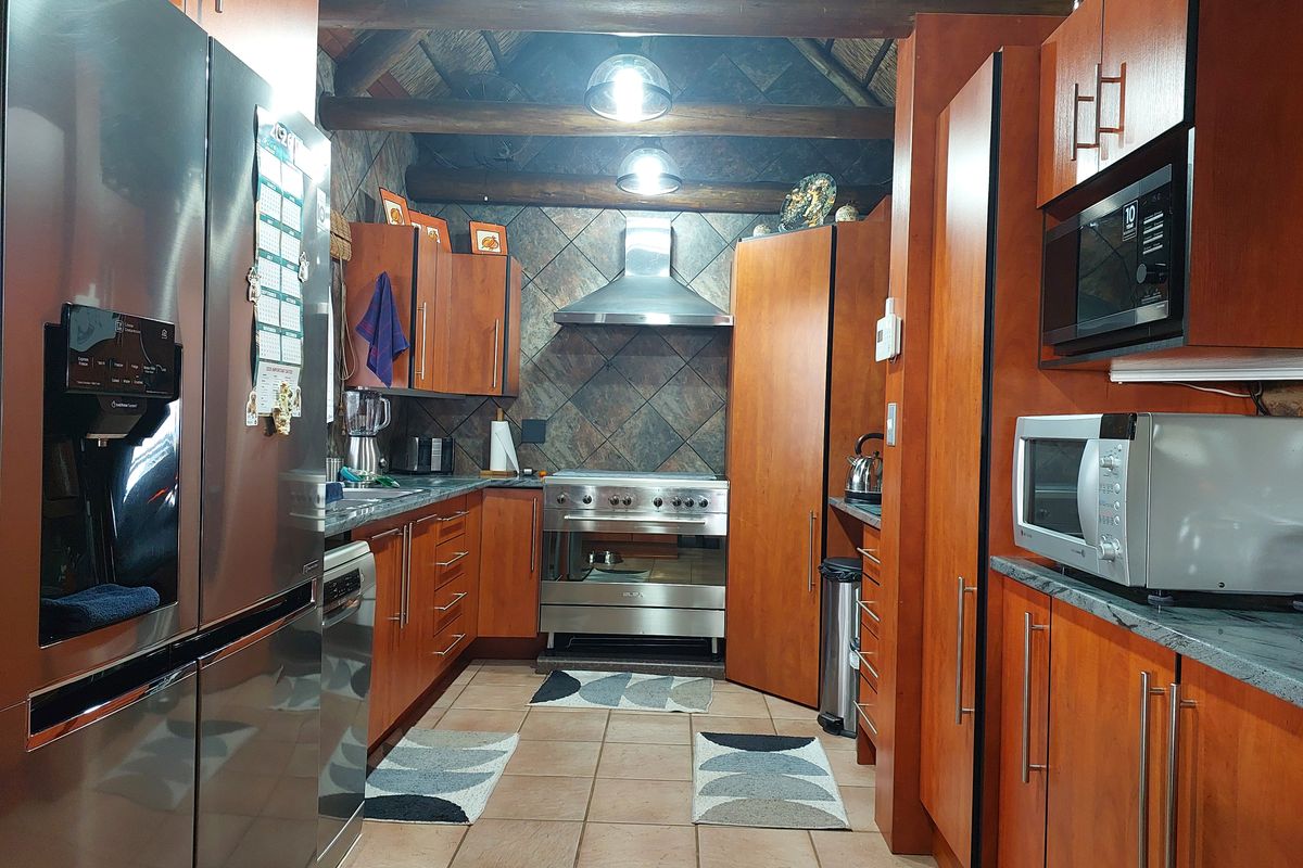 A functional kitchen featuring warm-toned wooden cabinetry, stone-look tile backsplash, stainless steel appliances, and a distinctive exposed timber beam ceiling.