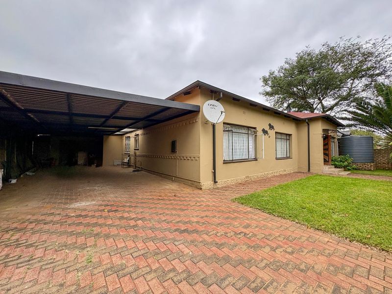Front exterior view of the house featuring a paved driveway, a large covered carport, and a well-maintained lawn area.