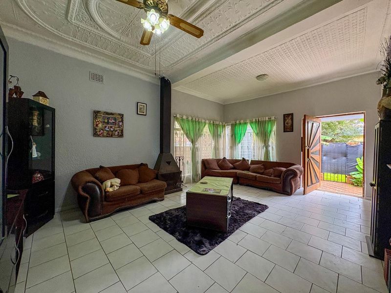 Spacious living room featuring a traditional fireplace, decorative pressed metal ceiling, and direct access to the outdoor area through a wooden door.