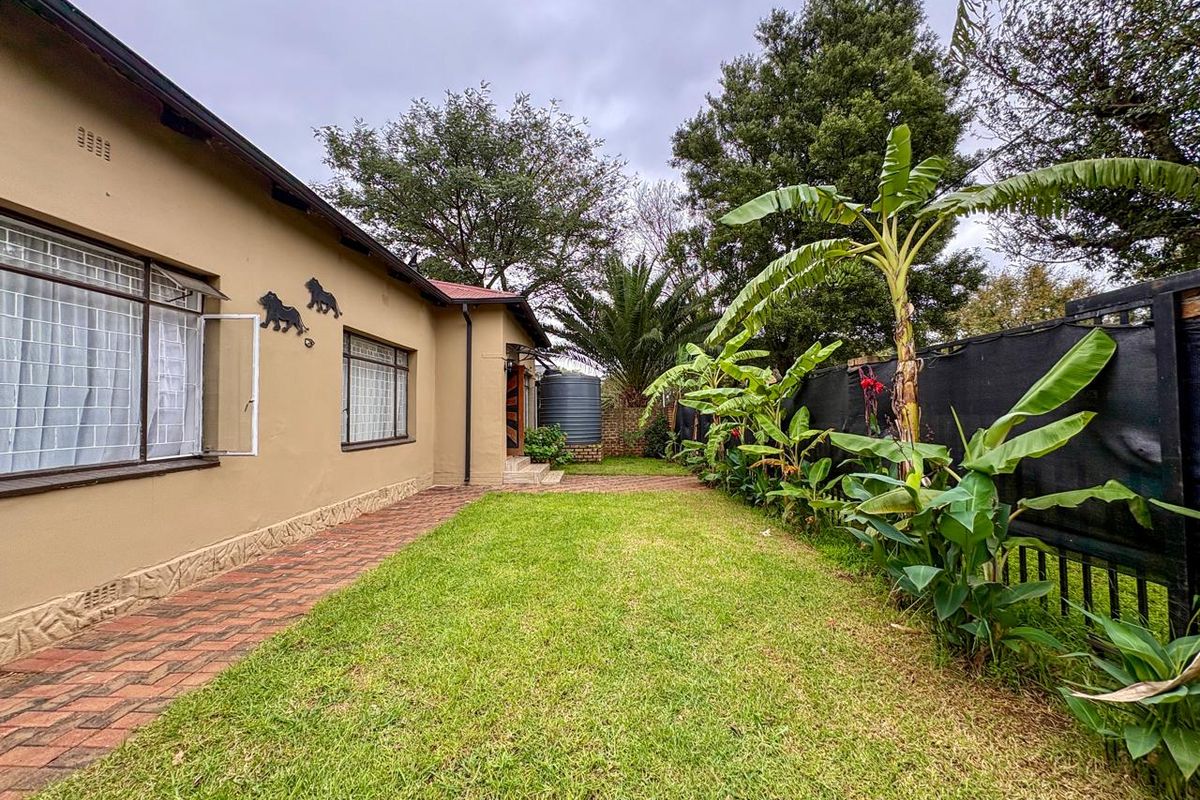 A well-maintained rear garden featuring a paved walkway, lush lawn, established banana trees, and a water storage tank against the house exterior.