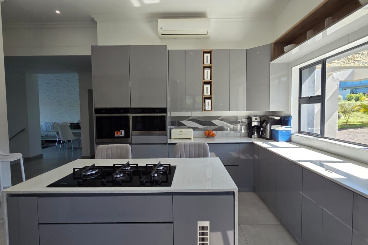 Modern kitchen featuring high-gloss grey cabinetry, stone countertops, a central island with a gas cooktop, and integrated built-in appliances.