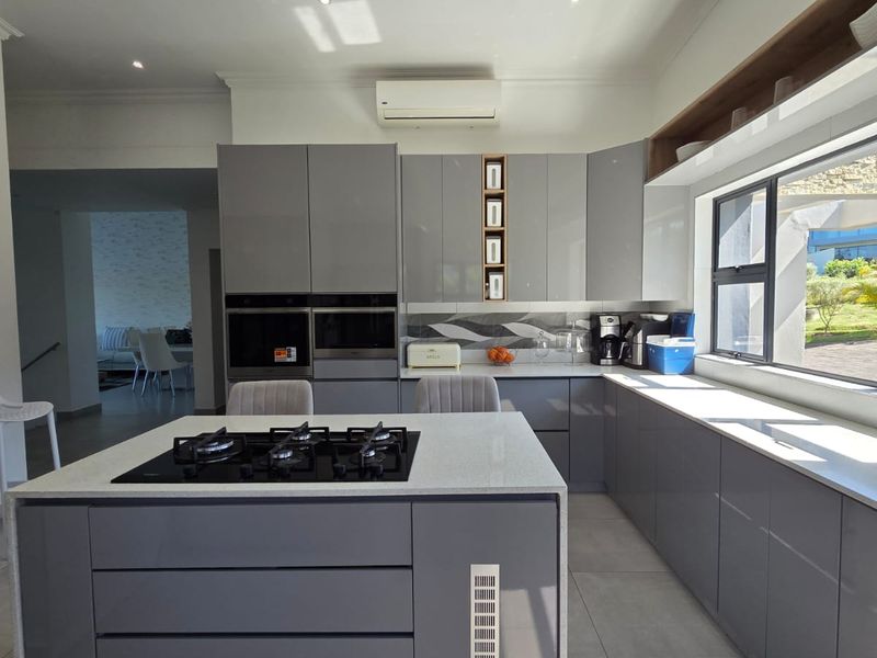 Modern kitchen featuring high-gloss grey cabinetry, stone countertops, a central island with a gas cooktop, and integrated built-in appliances.