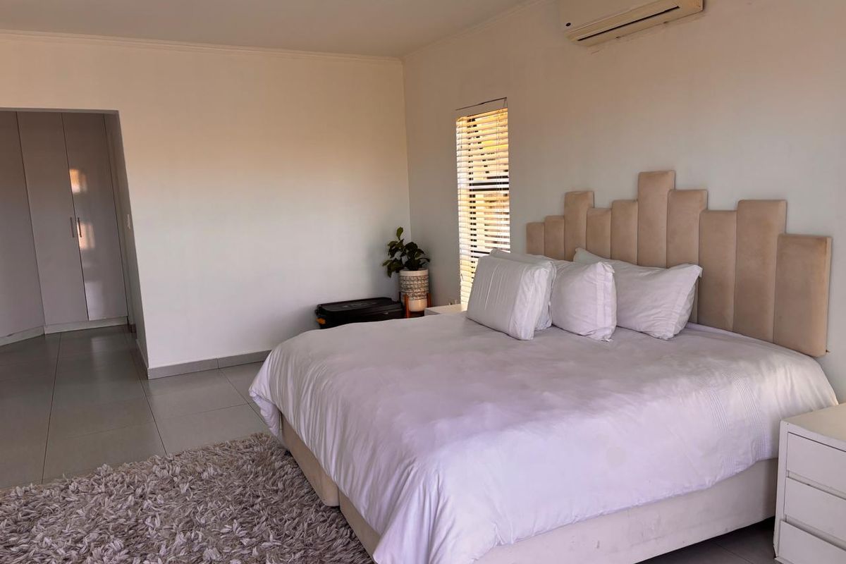 A spacious bedroom featuring tiled flooring, built-in cupboards, and a wall-mounted air conditioning unit, offering a clean and functional living space.
