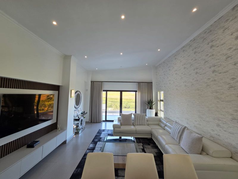 Spacious modern living room featuring a textured feature wall, built-in media cabinetry with timber detailing, recessed lighting, and large sliding doors leading to the outdoors.