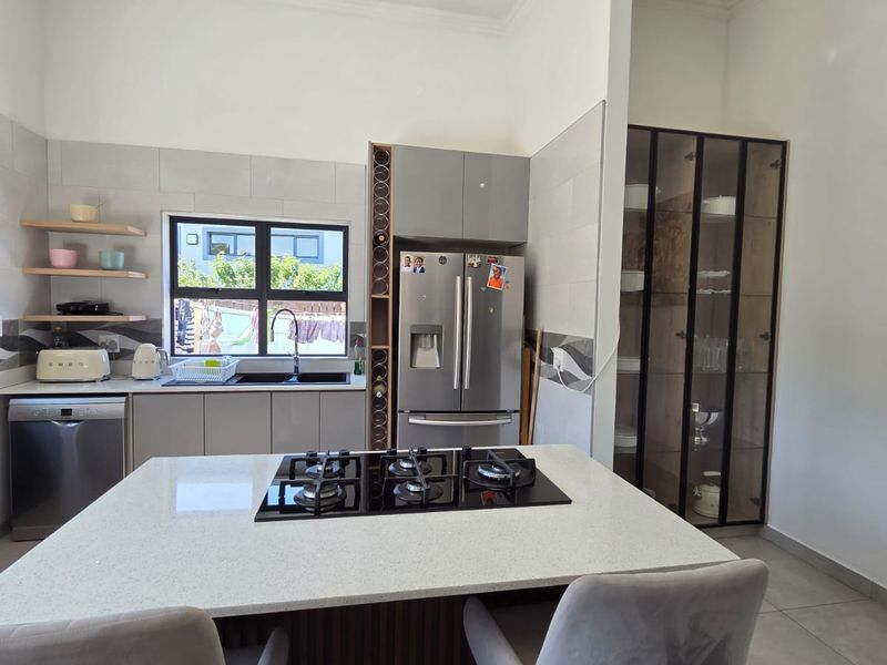 Modern kitchen featuring a central island with a gas cooktop, stone countertops, sleek cabinetry, and a built-in glass-front display cabinet.