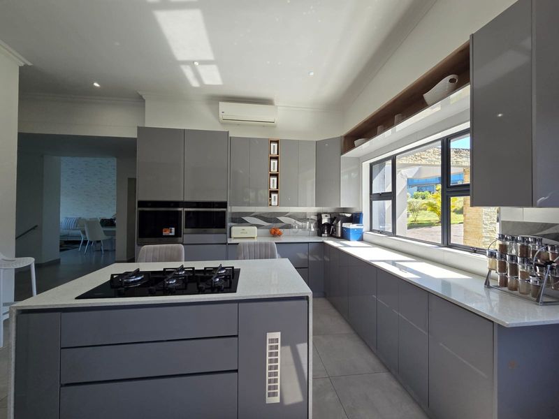 Modern kitchen featuring sleek grey cabinetry, stone countertops, a central island with a gas hob, and high-end built-in appliances.