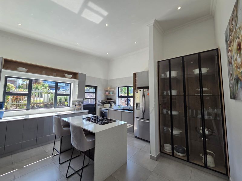 Modern kitchen featuring a central island with gas hob, sleek grey cabinetry, stone countertops, and a large built-in display cabinet.