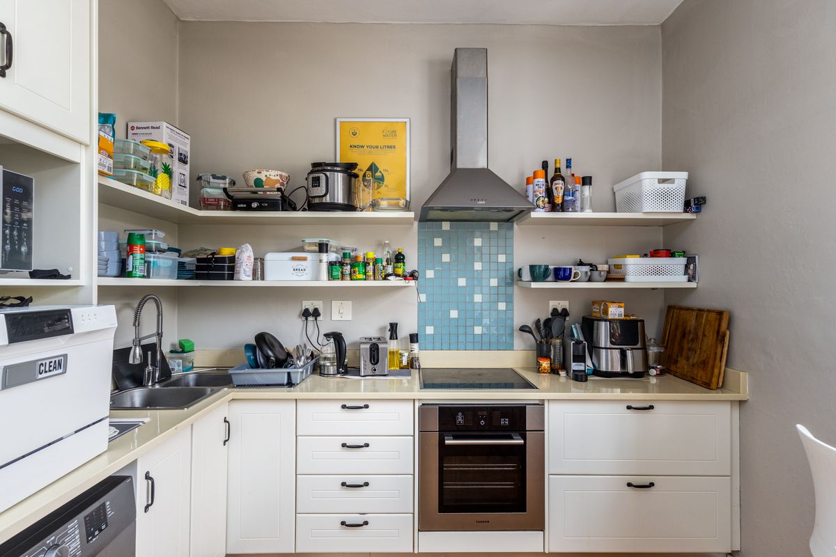 Compact kitchen featuring white cabinetry, a stainless steel oven, electric hob, extractor fan, and a blue mosaic tile splashback.