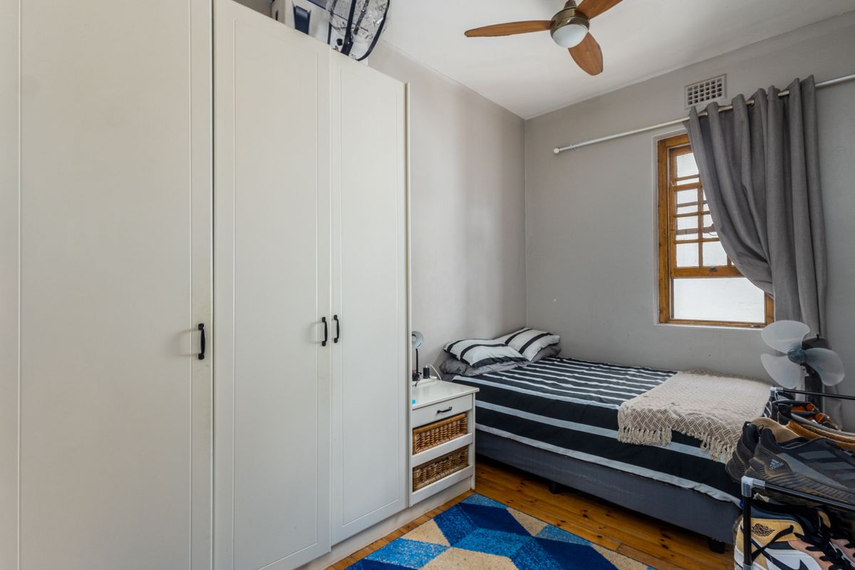 A compact bedroom featuring built-in white cabinetry, timber flooring, and a ceiling fan, providing functional storage and living space.