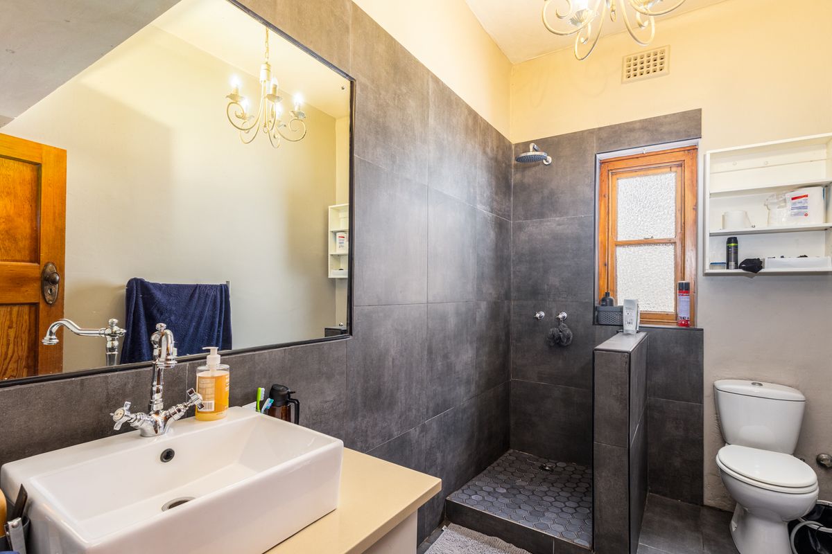 Modern bathroom featuring a walk-in shower with dark grey tiling, a vessel sink vanity, and a classic wooden window frame.