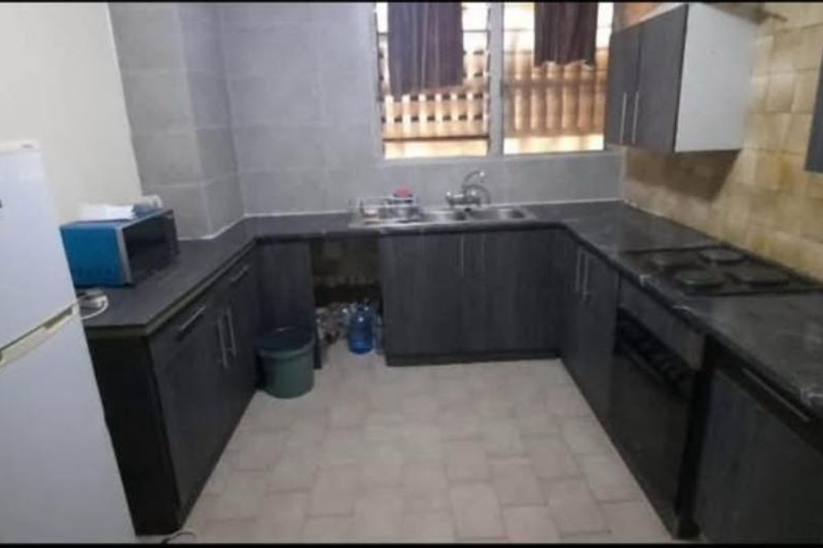 A functional U-shaped kitchen featuring dark cabinetry, stone-look countertops, a built-in oven, and a double-basin sink with tiled splashbacks.