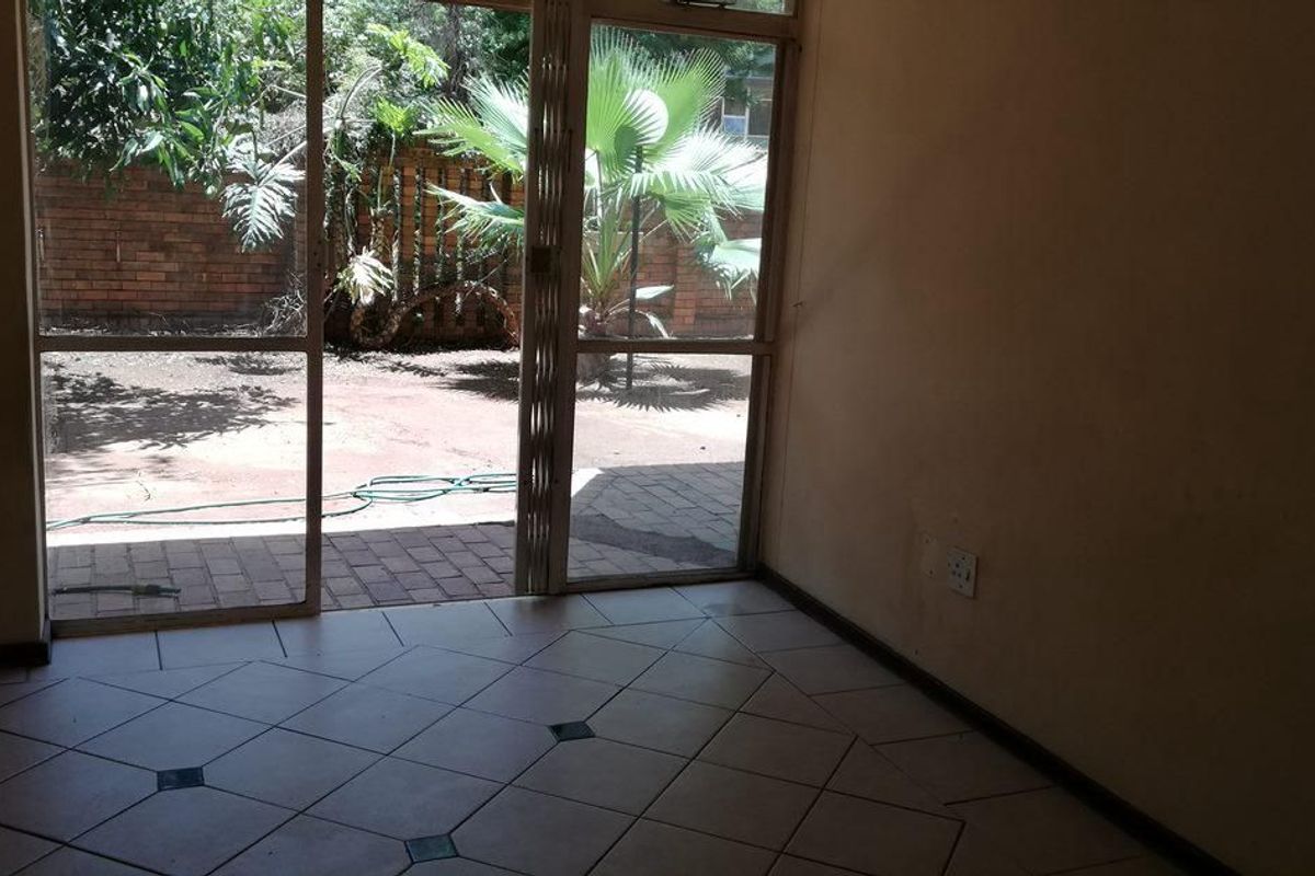 An empty living area featuring tiled flooring and large sliding glass doors that provide direct access to a private rear garden space.