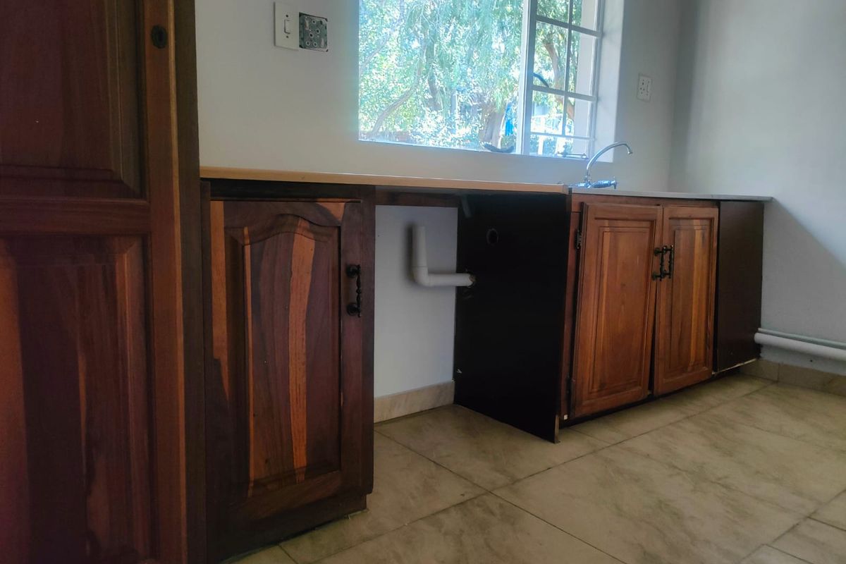 A dated kitchen area featuring wooden cabinetry, a single sink, and tiled flooring, currently requiring repairs to the cabinetry and exposed plumbing fixtures.