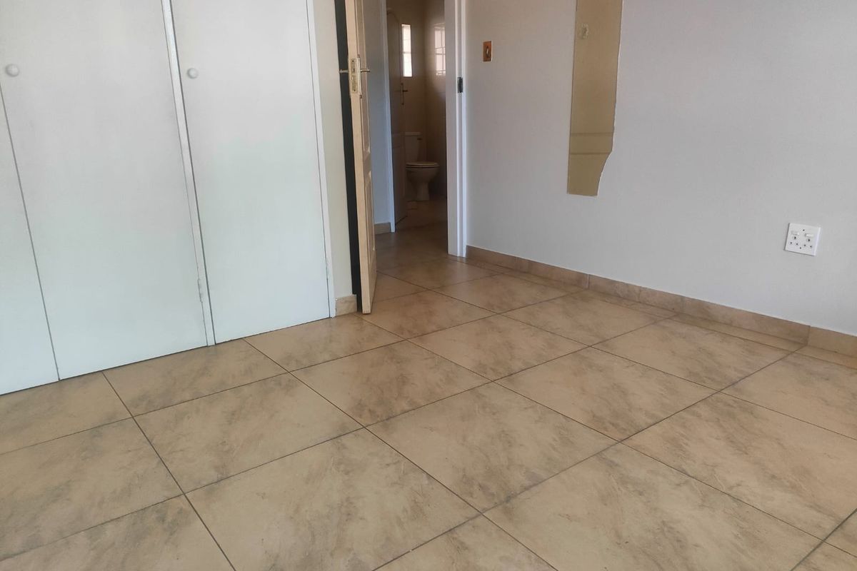 A vacant bedroom featuring tiled flooring, built-in cupboards, and direct access to an en-suite bathroom.