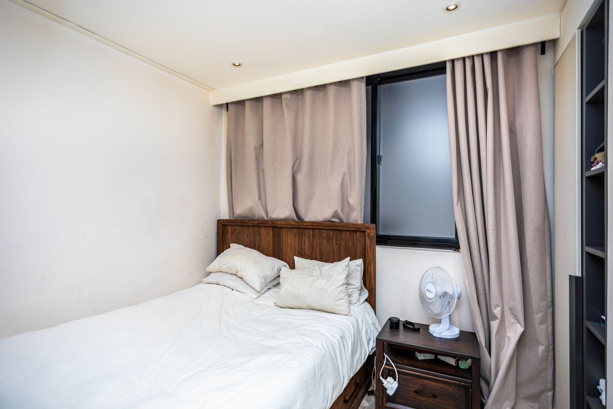 A compact bedroom featuring built-in shelving, recessed ceiling lighting, and a window with floor-to-ceiling curtains.