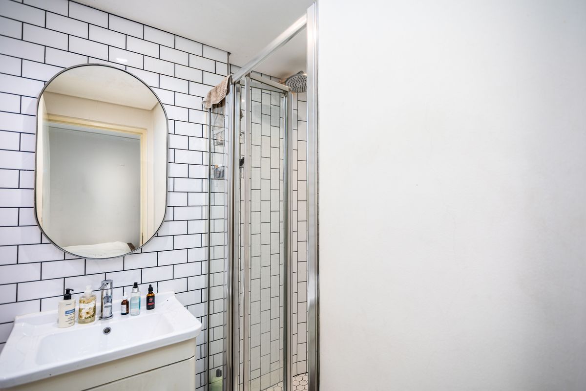 Modern bathroom featuring a white vanity, oval wall mirror, and a glass-enclosed shower with classic white subway tile backsplash.