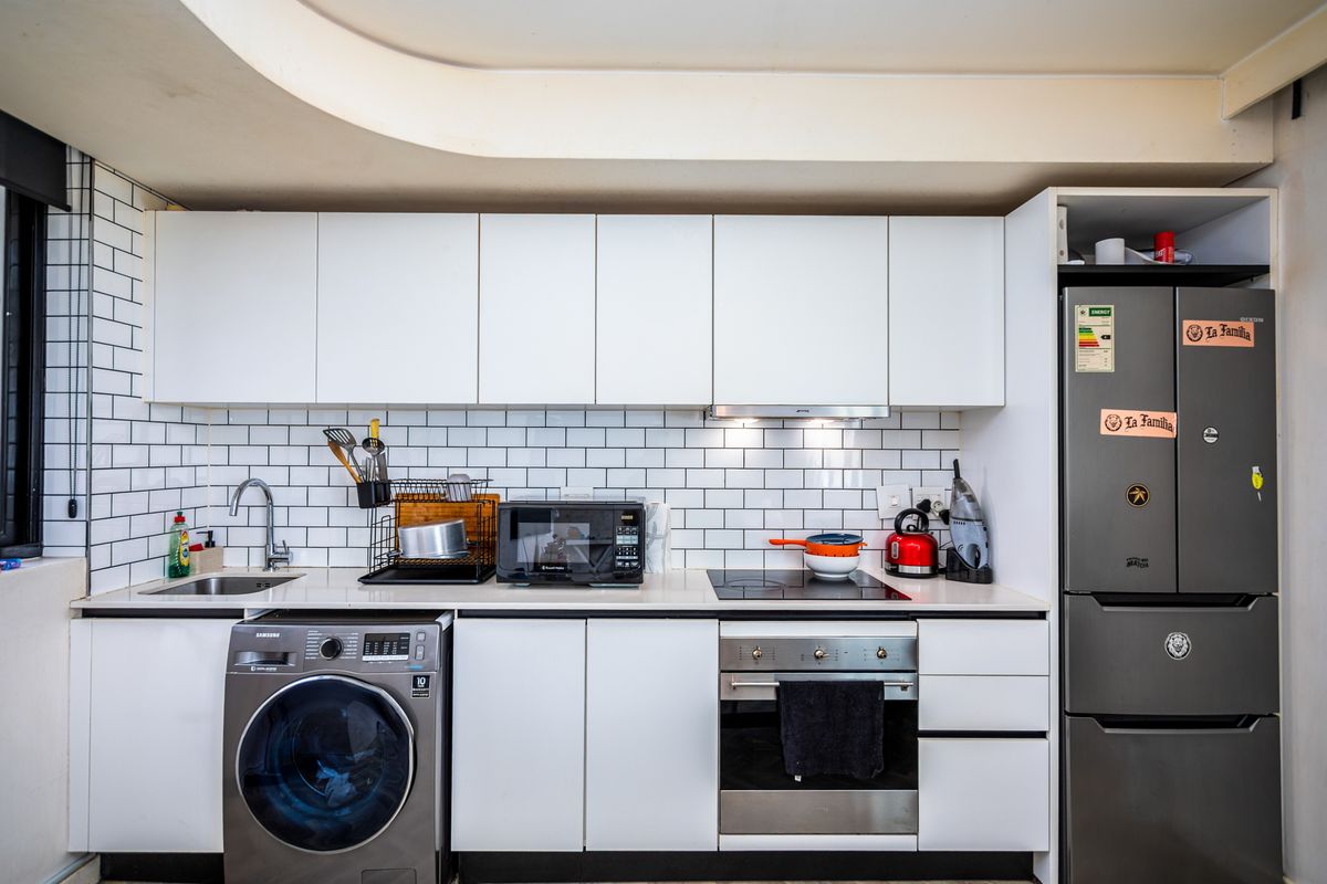 Modern kitchen featuring white cabinetry, subway tile backsplash, integrated oven, induction hob, extractor fan, and a built-in washing machine.