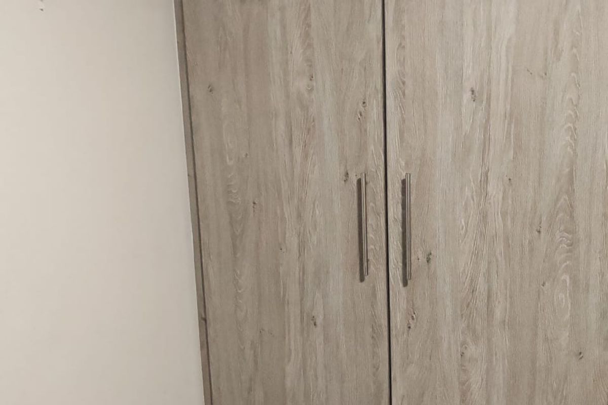 A built-in bedroom cupboard featuring a light wood-grain finish and modern metal handles.