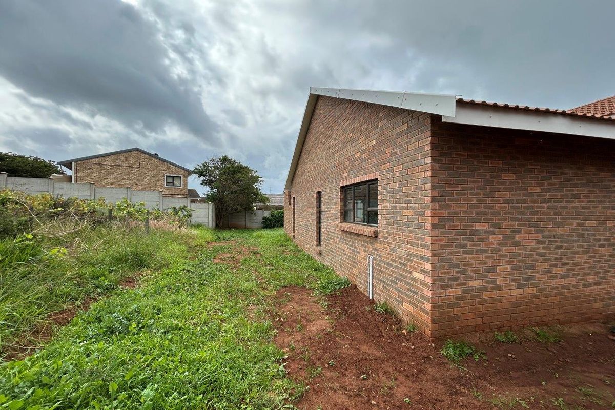 Rear view of the property featuring a face brick exterior, tiled roof, and an expansive, unlandscaped garden area enclosed by a precast concrete boundary wall.