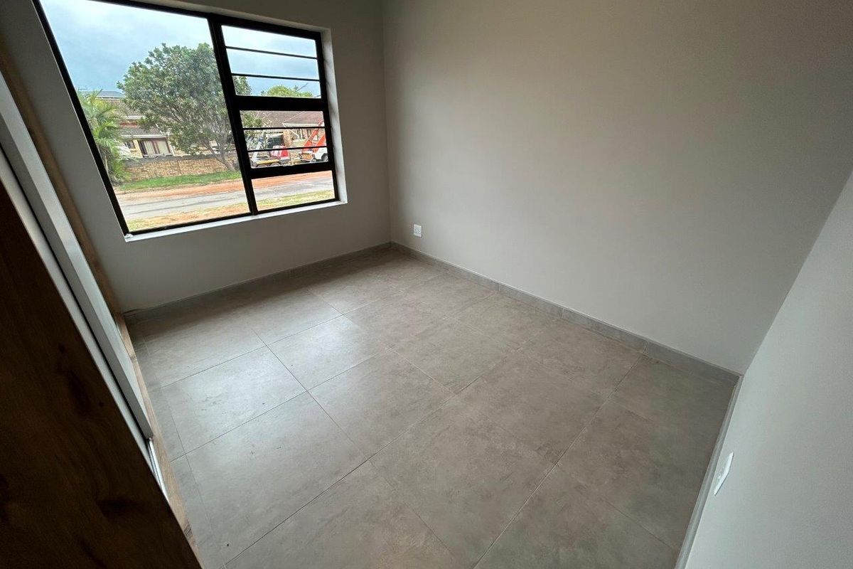 A clean, empty bedroom featuring modern neutral floor tiles and a large aluminium-framed window providing natural light.