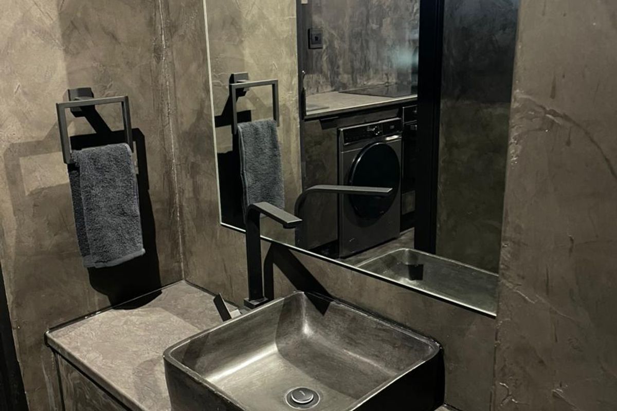 Modern bathroom featuring a dark vessel sink, black fixtures, and a sleek cement-finish aesthetic with a large integrated mirror.
