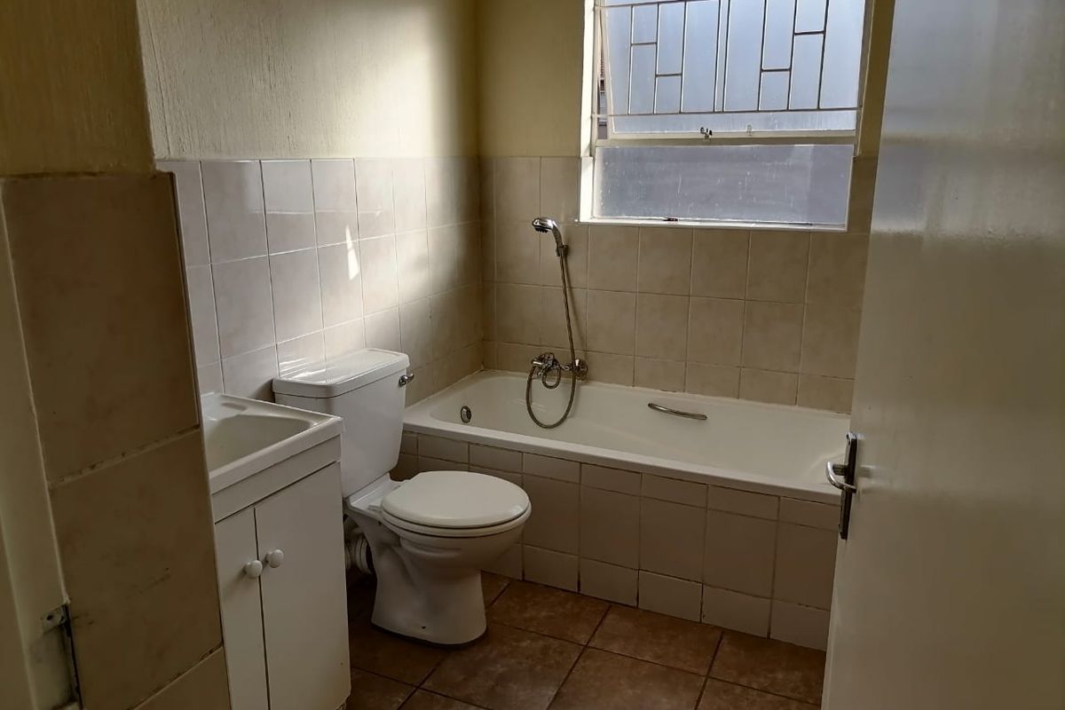 A functional bathroom featuring a bathtub with handheld shower, toilet, and vanity basin, finished with tiled walls and flooring.