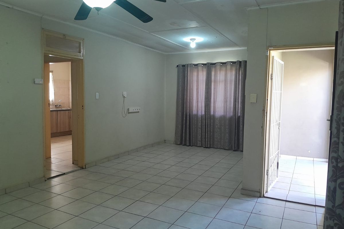 A spacious living area featuring tiled flooring, a ceiling fan, and direct access to adjacent rooms and an outdoor area.