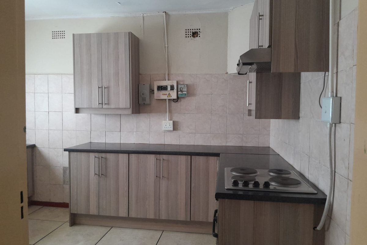 Functional kitchen featuring wood-look cabinetry, dark countertops, a built-in electric hob, and an extractor fan, with tiled splashbacks and flooring.