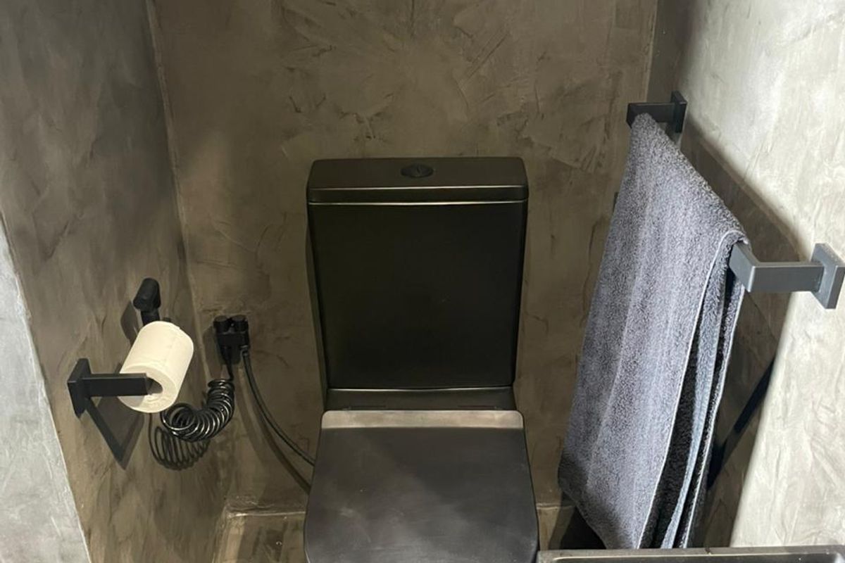 A modern bathroom featuring a matte black toilet, matching black hardware, and textured grey concrete-style wall and floor finishes.