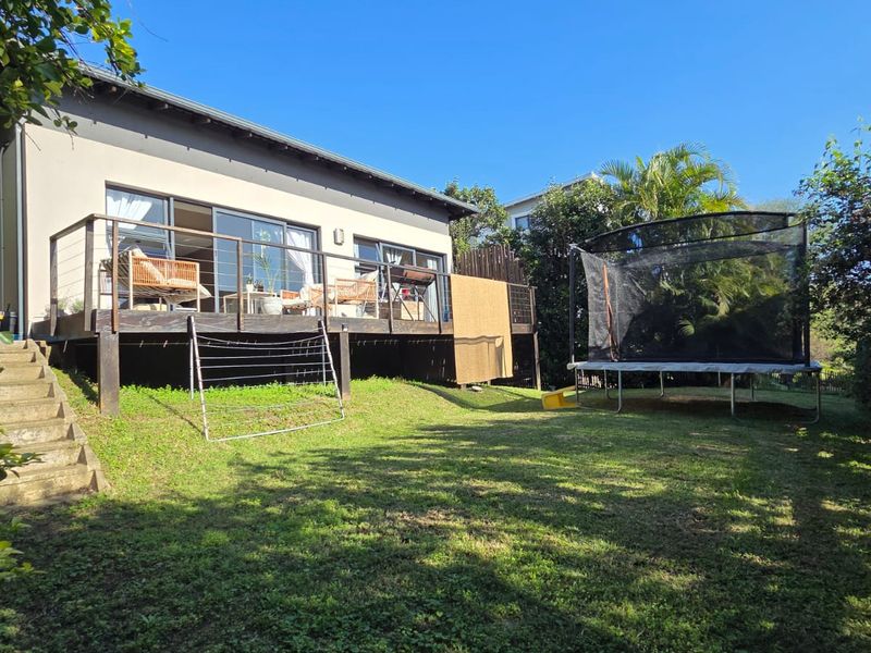 Rear view of the property featuring a raised timber deck with sliding glass doors and access stairs leading to a garden area.