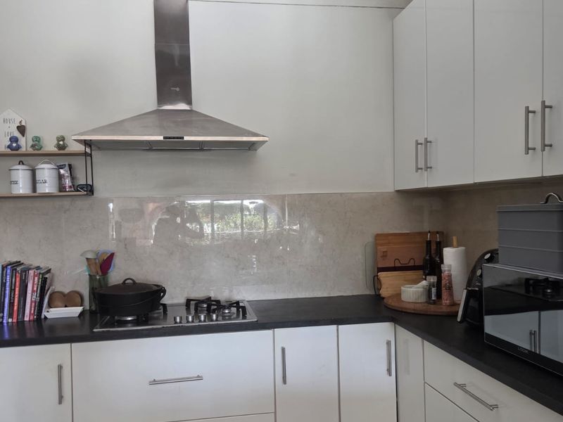 Modern kitchen featuring white cabinetry, dark countertops, a gas hob with stainless steel extractor fan, and neutral tiled flooring.